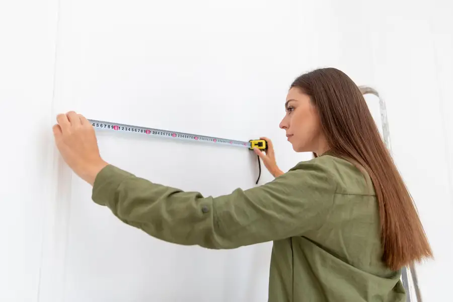 Woman using a tape measure on a window for installing shades